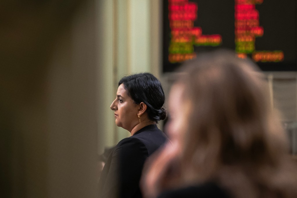An assemblymember on the assembly floor with a floor vote screen in the background.