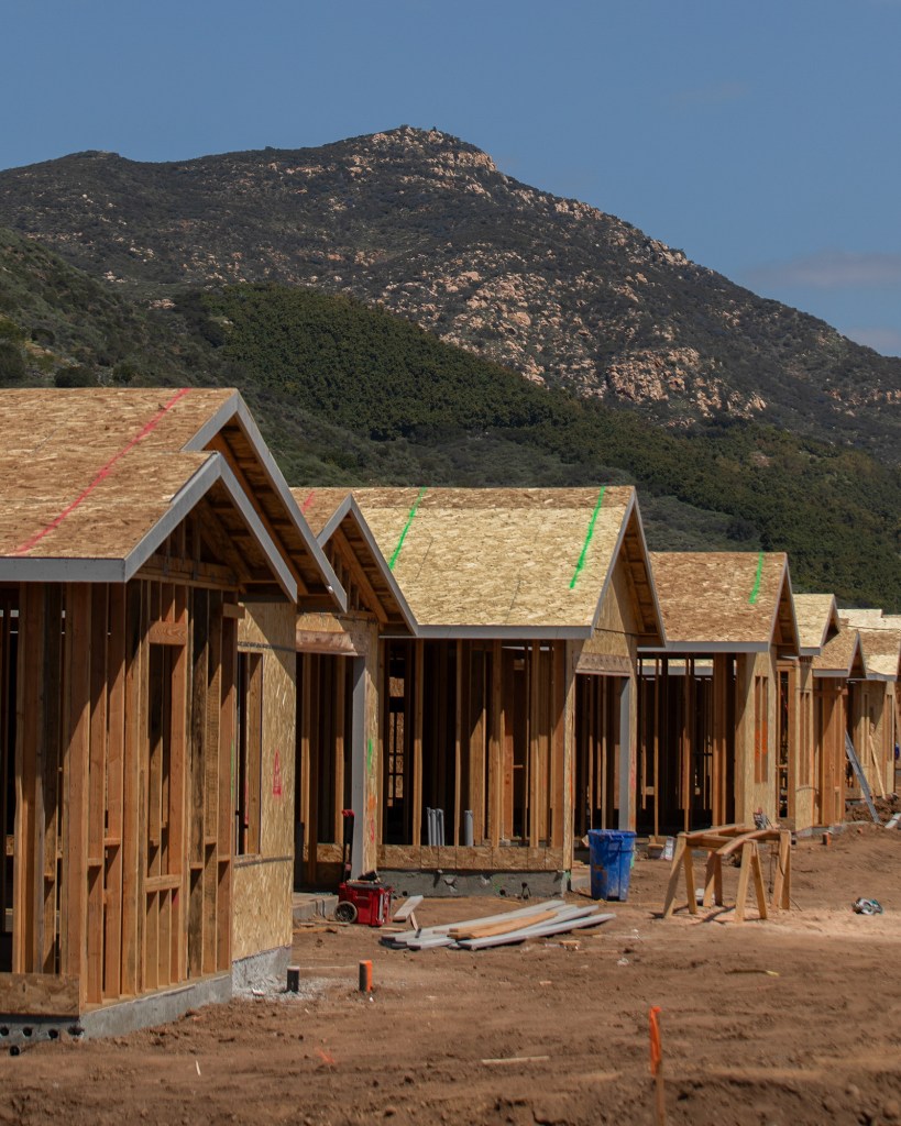 A row of single-family homes under construction set against the background of small hills.