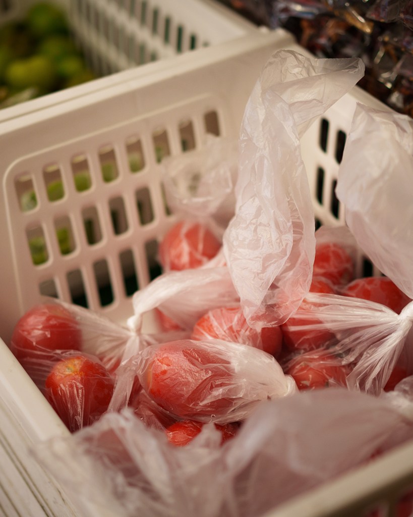 A close-up view of tomatoes wrapped in plastic bags inside a small container at a grocery store.