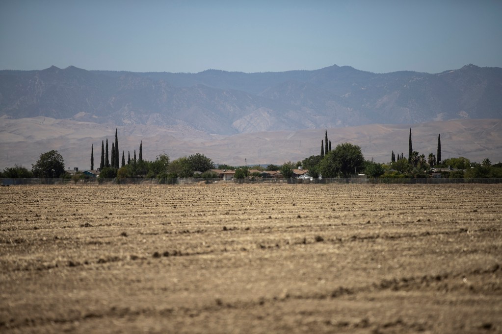 A view of the town of Cantua Creek across from an agricultural field with a view of a mountain range in the distance.