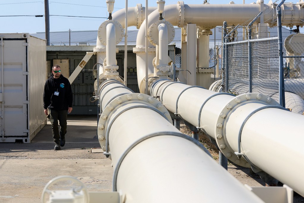 A person walks next to two large and white water pipe structures at a port.