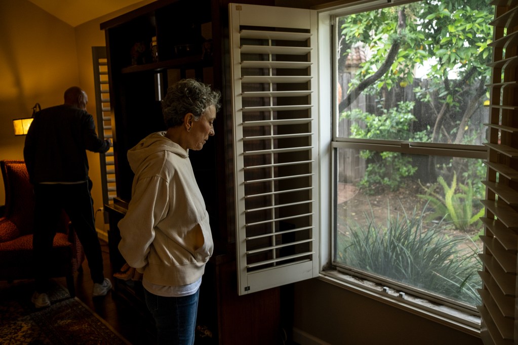 A person stands in front of a window with open shutters as they look down.