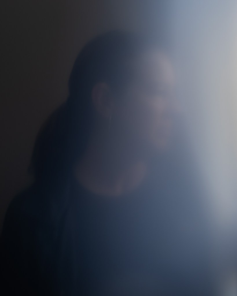 A blurred view of a person's silhouette as they look out a window.