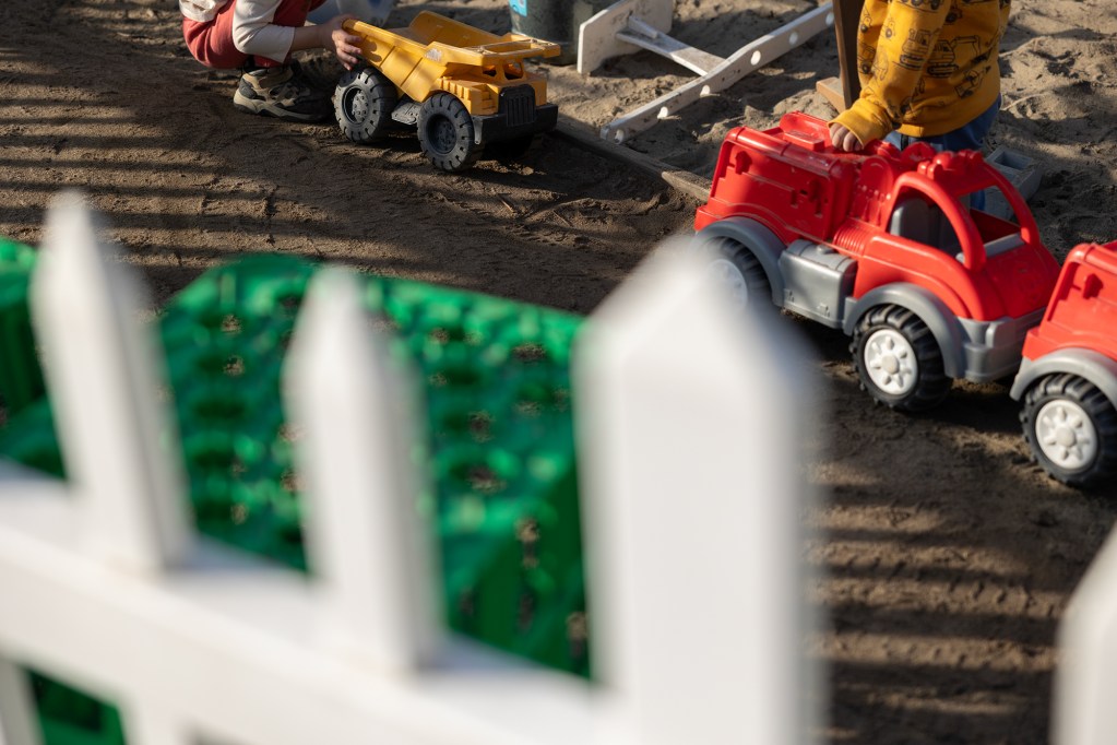 A detailed look of two unidentifiable toddlers playing with toy trucks at a playground.