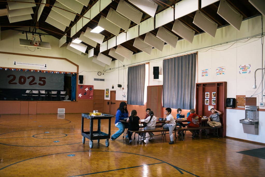 Nine young children sit on a single table inside a school gym