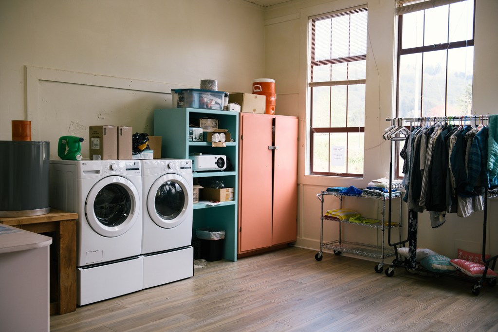 A room with washer, dryer, clothing rack and other items.