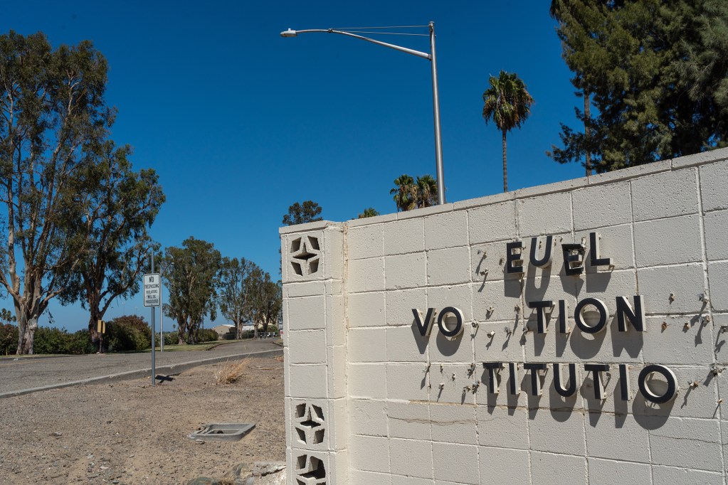 A worn-out sign on a concrete wall with destroyed and missing letters near the entrance of a closed-down prison.