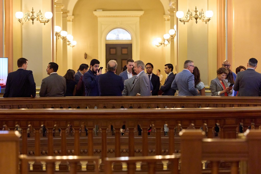 A crowd of people, dressed in suits and business wear, stand and talk amongst each other in the rotunda area of a building.