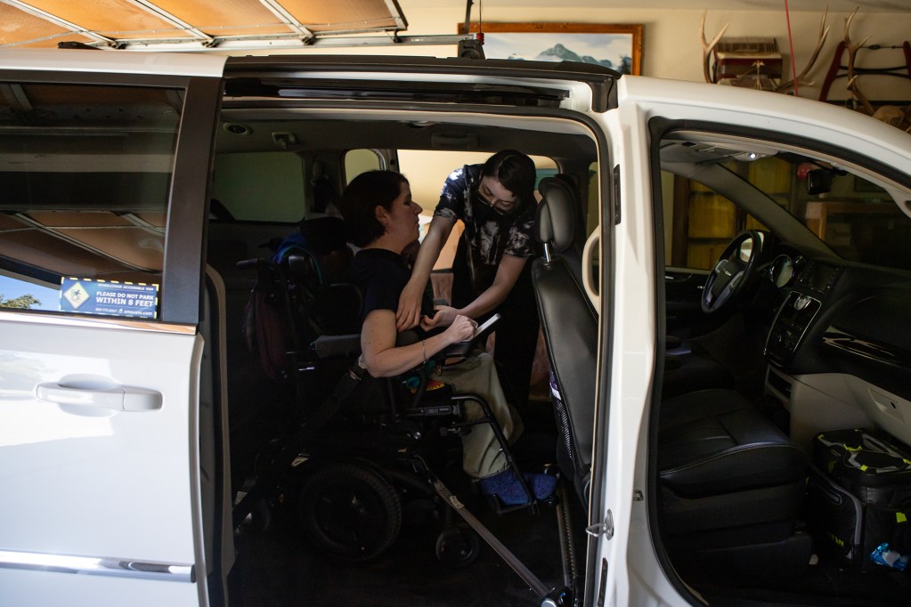 A person helps secure another person in a wheelchair inside a van.